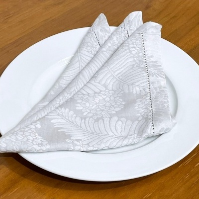 Guardanapo branco dobrado sobre prato branco numa mesa de madeira