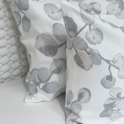 Almofadas brancas com padrão de folhas cinza e bege sobre superfície e fundo branco texturizado