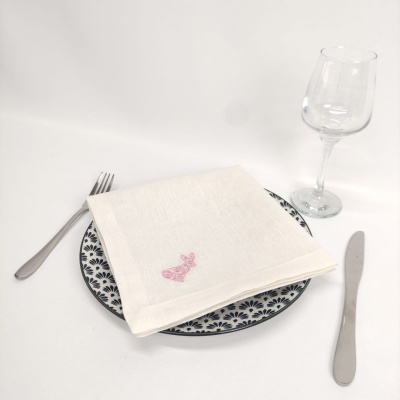 Conjunto de jantar com prato preto e branco, guardanapo branco bordado, talheres metálicos e copo de vidro.