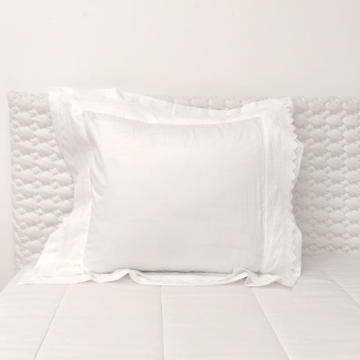 Almofada branca com friso rendado sobre cama branca com cabeceira acolchoada