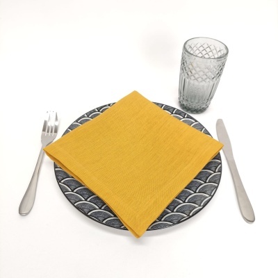 Mesa posta com prato cinza, guardanapo amarelo, talheres de metal e copo de vidro