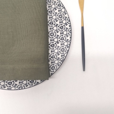 Prato branco com padrão azul, guardanapo verde oliva e utensílio com cabo cinza e amarelo