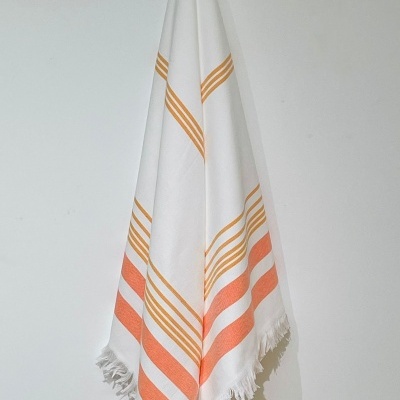 Toalha branca com riscas laranja e amarelas pendurada, com franjas