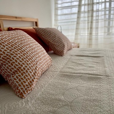 Cama com colcha bege texturizada e almofadas castanhas e brancas com padrão geométrico