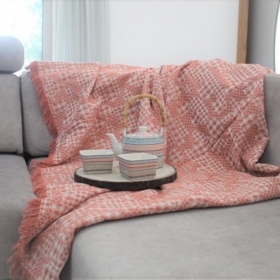 Cobertor vermelho e branco com pote e caixas decorativas sobre sofá cinzento