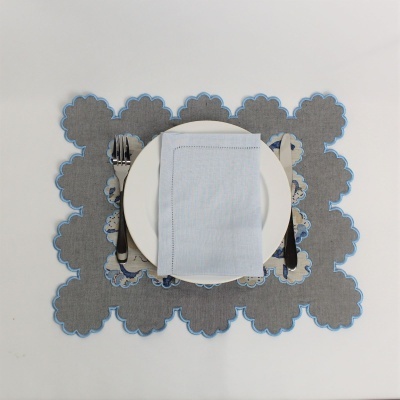 Mesa posta com prato branco, guardanapo azul, talheres metálicos e placemat cinzento com borda azul