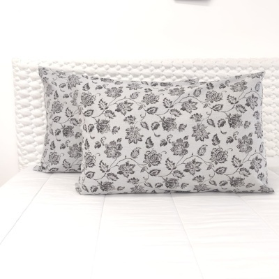 Almofadas brancas com padrão floral preto sobre cama branca texturada