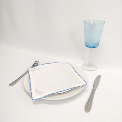 Prato branco com guardanapo branco bordado azul, talheres metálicos e copo azul claro