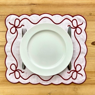 Prato branco em pano bordado branco e vermelho com garfo e faca numa mesa de madeira