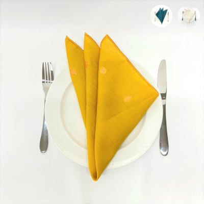 Guardanapo amarelo com círculos cor-de-rosa sobre prato branco, garfo e faca ao lado sobre fundo branco