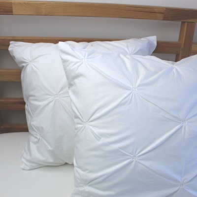 Duas almofadas brancas texturizadas sobre superfície branca com estrutura de madeira ao fundo