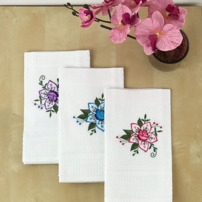 Toalhas de tecido branco com bordados florais coloridos e planta com flores cor de rosa
