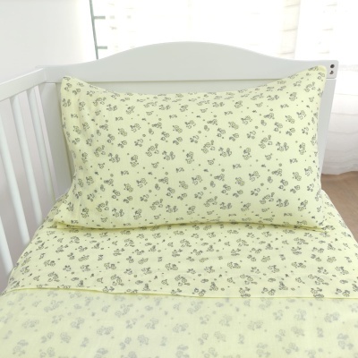 Conjunto de roupa de cama amarilla clara com padrão de flores cinza num berço branco