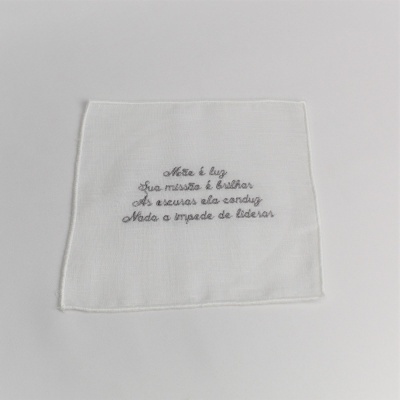 Pano branco quadrado com bordado em cinza e texto em português.
