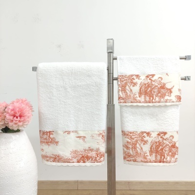 Toalhas brancas com detalhes em terracota num suporte metálico ao lado de um vaso com flor rosa