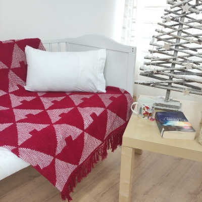 Cobertor vermelho e branco com padrão de árvores numa sala com sofá branco e mesa com caneca e livro.