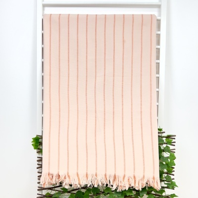 Toalha cor de rosa claro com riscas verticais finas e franjas pendurada numa estrutura branca com plantas verdes.