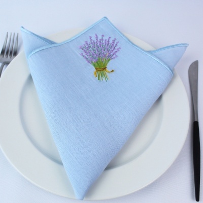 Guardanapo azul claro bordado com ramo de lavanda sobre prato branco com talheres ao lado