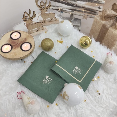 Toalhas de Natal verdes com motivos brancos, velas, bolas decorativas douradas e brancas, renas e gnomos de Natal num ambiente festivo branco.