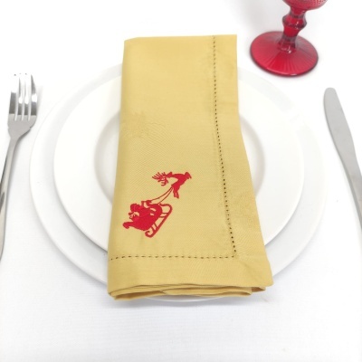 Guardanapo amarelo com bordado vermelho num prato branco com talheres e copo
