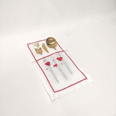 Guardanapo branco com bordas vermelhas, corações vermelhos e talheres dourados em cima