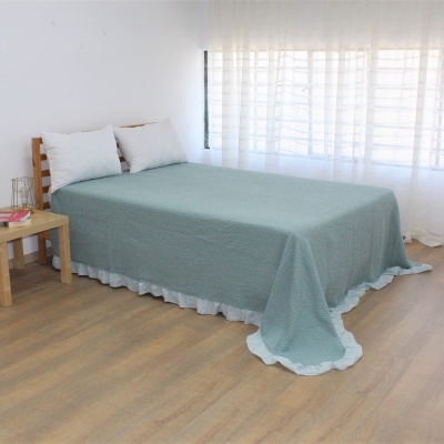 Cama de madeira com colcha verde e almofadas brancas num quarto com cortinas brancas