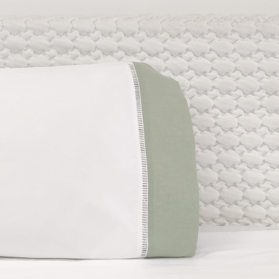 Fronha branca com borda verde clara e padrão texturado no colchão