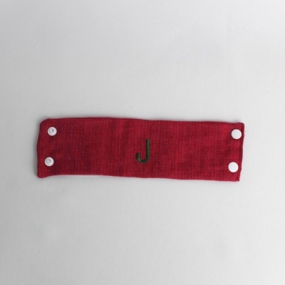 Faixa vermelha em tecido com botões brancos e letra J verde bordada