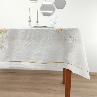 Toalha de mesa branca bordada com detalhes dourados em mesa de madeira