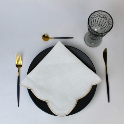 Conjunto de jantar com prato preto, guardanapo branco, talheres dourados e pretos e copo cinzento com padrão