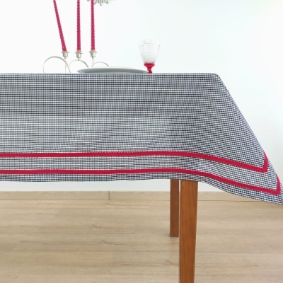 Toalha de mesa xadrez preta e branca com borda vermelha sobre mesa de madeira.