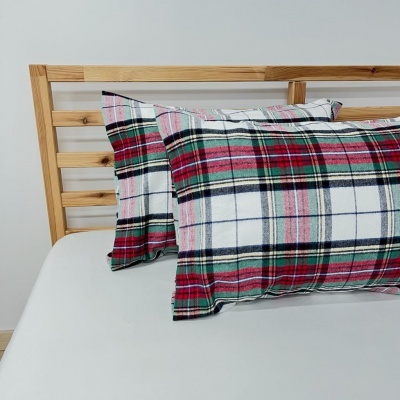 Almofadas com fronhas xadrez vermelho, branco, preto e verde numa cama com cabeceira de madeira clara.