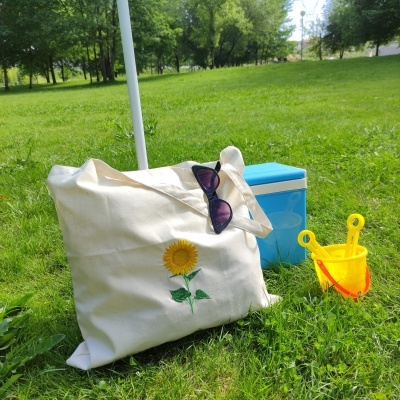 Bolsa com bordado de girassol, óculos de sol, caixa térmica azul e balde de praia amarelo no relvado verde