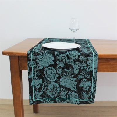 Toalha de mesa com padrão floral azul turquesa sobre fundo preto com louça e taça