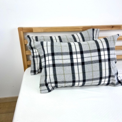 Duas almofadas decorativas xadrez cinzento e branco numa cama branca com estrutura de madeira