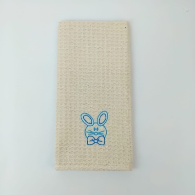 Toalha bege com bordado azul de coelho e textura bolha