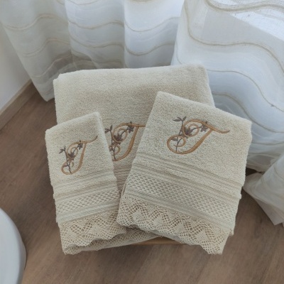 Toalhas bege com bordados dourados e renda em chão de madeira com cortina branca ao fundo