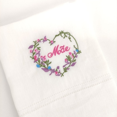 Toalha branca com bordado floral em forma de coração e a palavra 'Mãe' no centro
