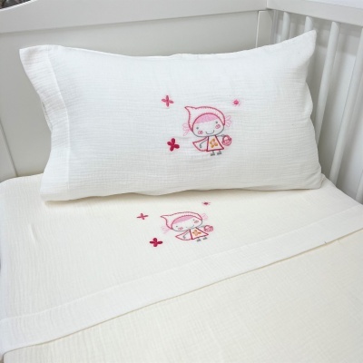 Conjunto de almofada e lençol branco com bordado infantil rosa e vermelho numa cama de bebé