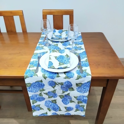 Toalha de mesa floral azul e verde numa mesa de madeira com pratos e copos