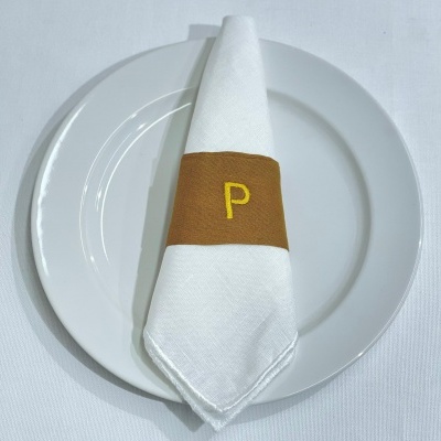 Guardanapo branco com banda castanha e letra P sobre prato branco
