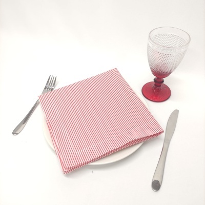 Conjunto de jantar com prato branco, guardanapo riscado vermelho e branco, talheres inox e copo de vidro com base vermelha