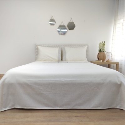 Cama de casal com roupa de cama branca e almofadas cinza claras com cabeceira texturizada e espelhos na parede