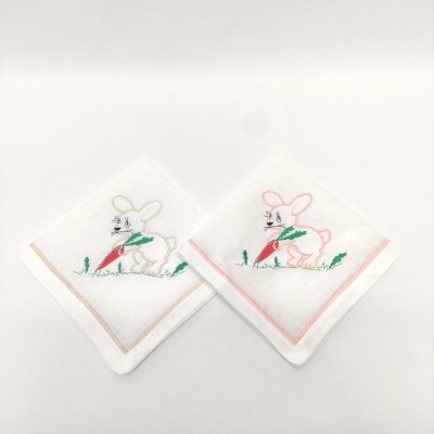 Dois panos brancos com bordados de coelho segurando cenoura, borda bege e borda cor-de-rosa