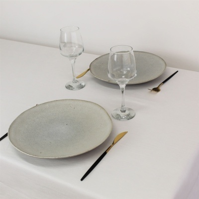 Mesa posta com pratos cinzentos, copos de vinho e talheres pretos e dourados