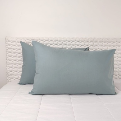 Duas almofadas azuis claras sobre cama branca com cabeceira texturada blanca