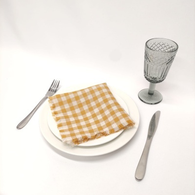 Conjunto de jantar com prato branco, guardanapo xadrez amarelo, talheres em inox e copo cinza texturizado.