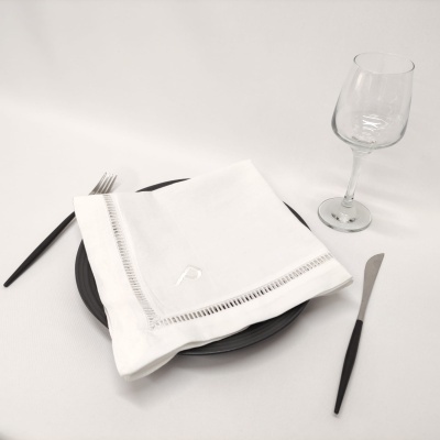 Guardanapo branco com bordado sobre prato preto com talheres e copo