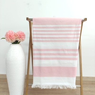 Toalha rosa e branca com riscas pendurada em estrutura de madeira ao lado de vaso branco com flores