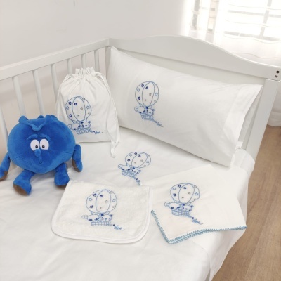 Conjunto de roupa de cama para bebé com bordados azuis e peluche azul num berço branco